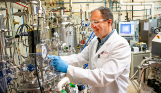 photo of man in lab with tubes, gauges, equipment, monitor