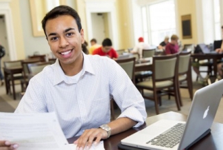 student in classroom with laptop and paper