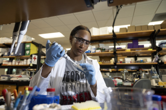 photo of woman working in lab with pipette, gloves, safety glasses