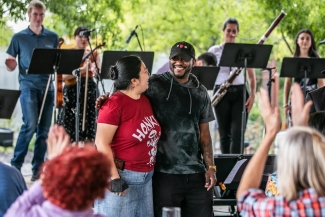 photo of musicians with instruments and music stands, two people in foreground