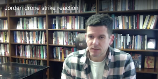 still photo of man, with bookshelves in background