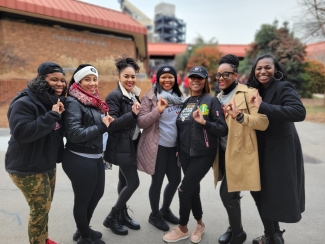 photo of seven women outdoors, with stadium in background