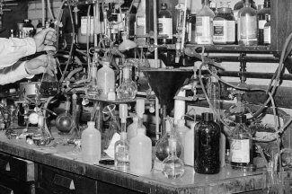 black white photo of beakers and test tubes, arms of a man