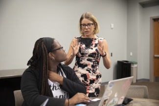 photo of professor standing and seated woman with laptop computer