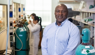 photo of man in lab, with people in lab coats, equipment in background