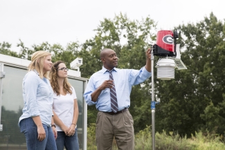 photo of man, two women, and rain/wind gauge, outdoors, 