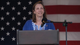 photo of woman at podium, American flag in background