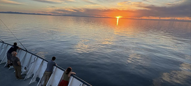photo of sunset on ocean, with people at rail of ship