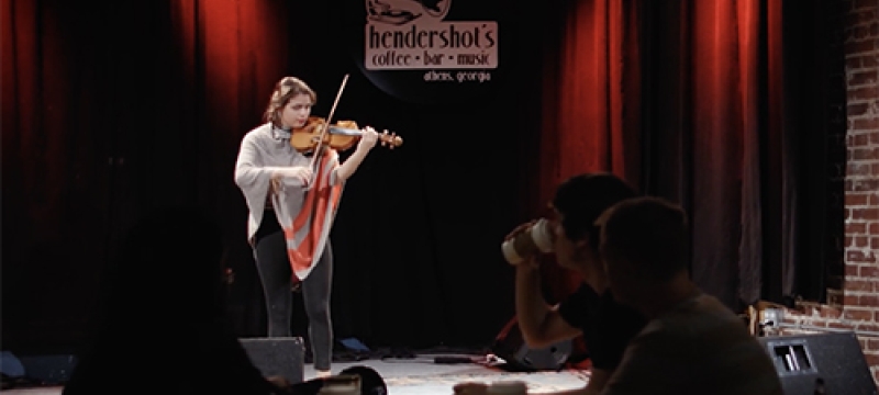 still photo of woman playing violin on a club stage