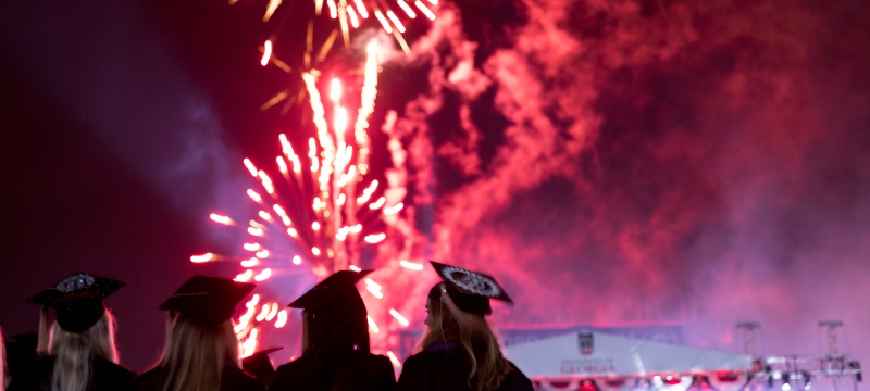 photo of people in caps and gowns, with fireworks in background