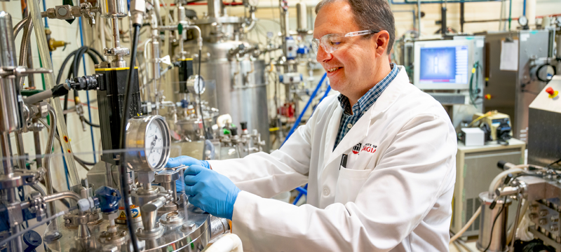 photo of man in lab with tubes, gauges, equipment, monitor