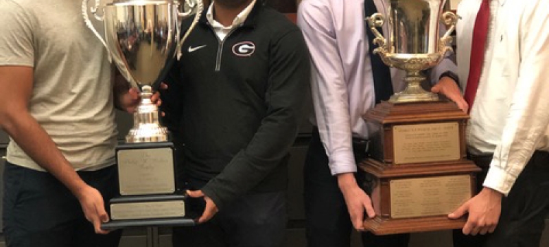 photo of four men holding two trophies 