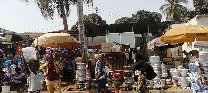 Photo of outdoor marketplace with goods, umbrellas, people and palm trees