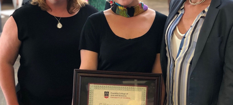 photo of three women, the middle holding a framed certificate
