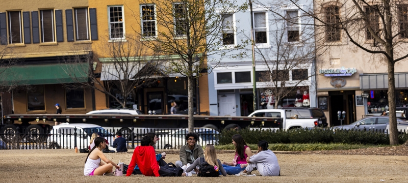 photo of people sitting in grass, day, downtown in background