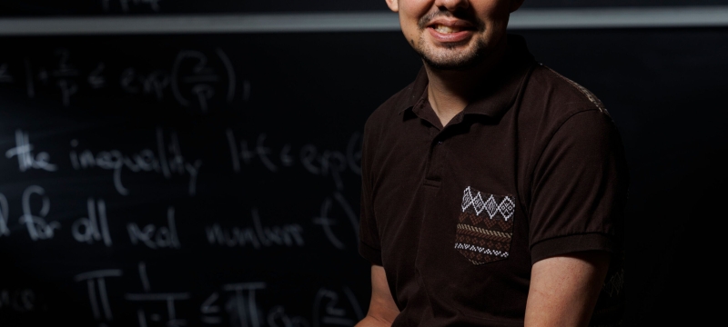 photo of man, chalkboard with letters and numerals in background