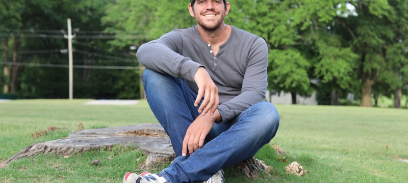 photo. of man sitting outside on tree stump