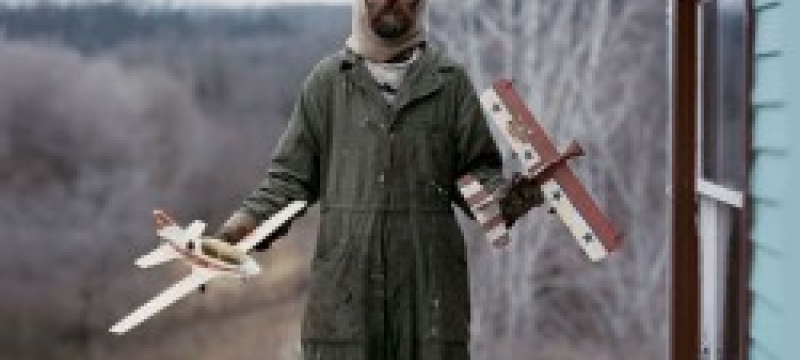 man with model airplanes on porch.