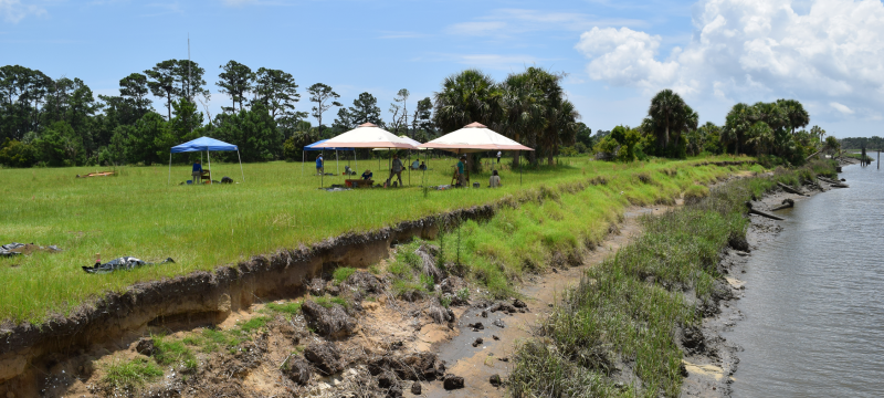 photo of shoreline, with grass, tents, and water, day