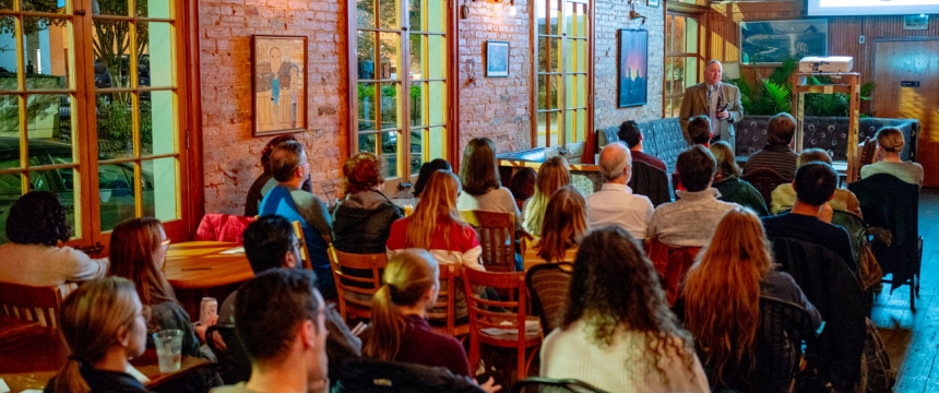 photo of man speaking to seated crowd in a coffee house