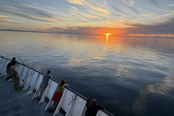 photo of sunset on ocean, with people at rail of ship