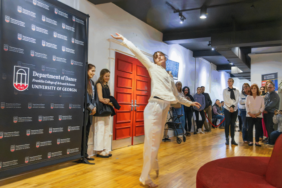 woman dances in room, people and banner in background.