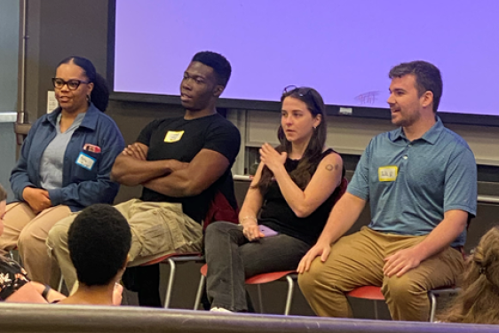 photo of four people seated with name tags, audience