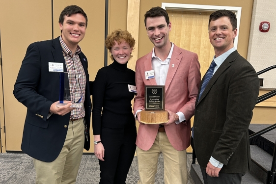 photo of four people, one holding a trophy