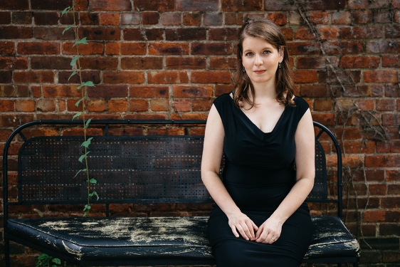 photo of woman sitting on a bench in front of brick wall