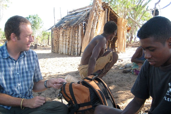 photo of three men with hut in background, day