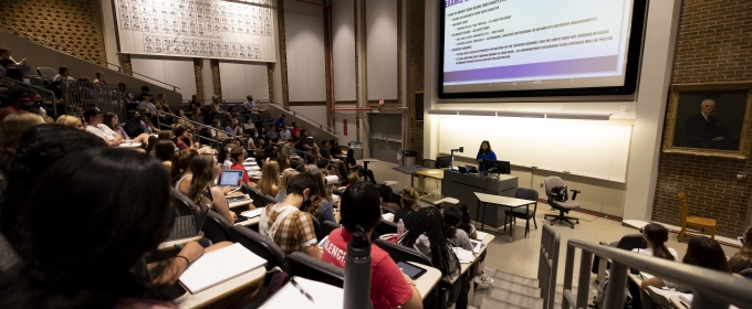 photo of lecture hall with students, screens