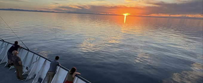 photo of sunset on ocean, with people at rail of ship