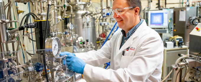 photo of man in lab with tubes, gauges, equipment, monitor