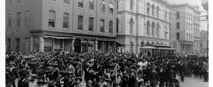 black and white historical photo of people marching on a city street