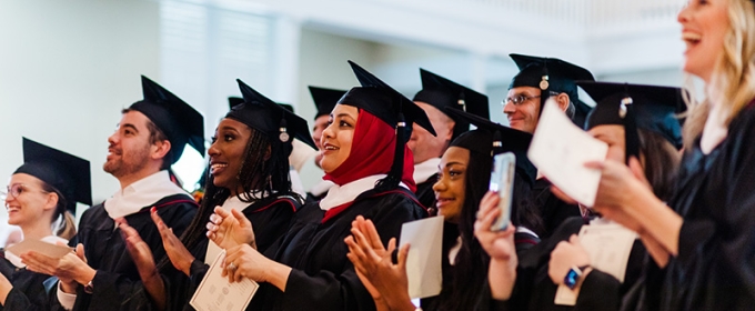 students standing and clapping in cap and gown