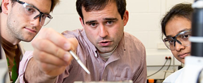 professor in lab, flanked by two students