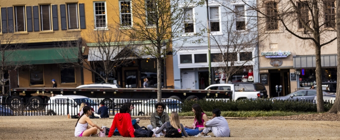 photo of people sitting in grass, day, downtown in background