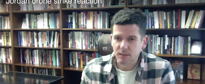 still photo of man, with bookshelves in background