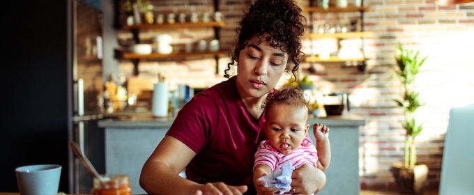 photo of woman holding baby, with laptop in kitchen