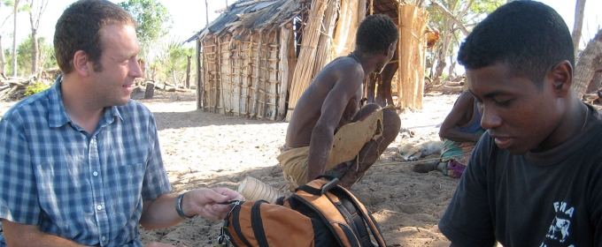 photo of three men with hut in background, day