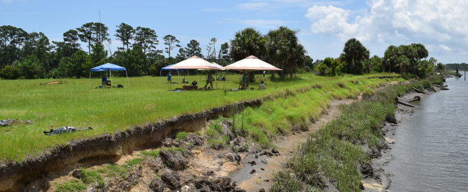 photo of shoreline, with grass, tents, and water, day