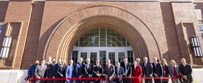 photo of group cutting ribbon in front of building, day